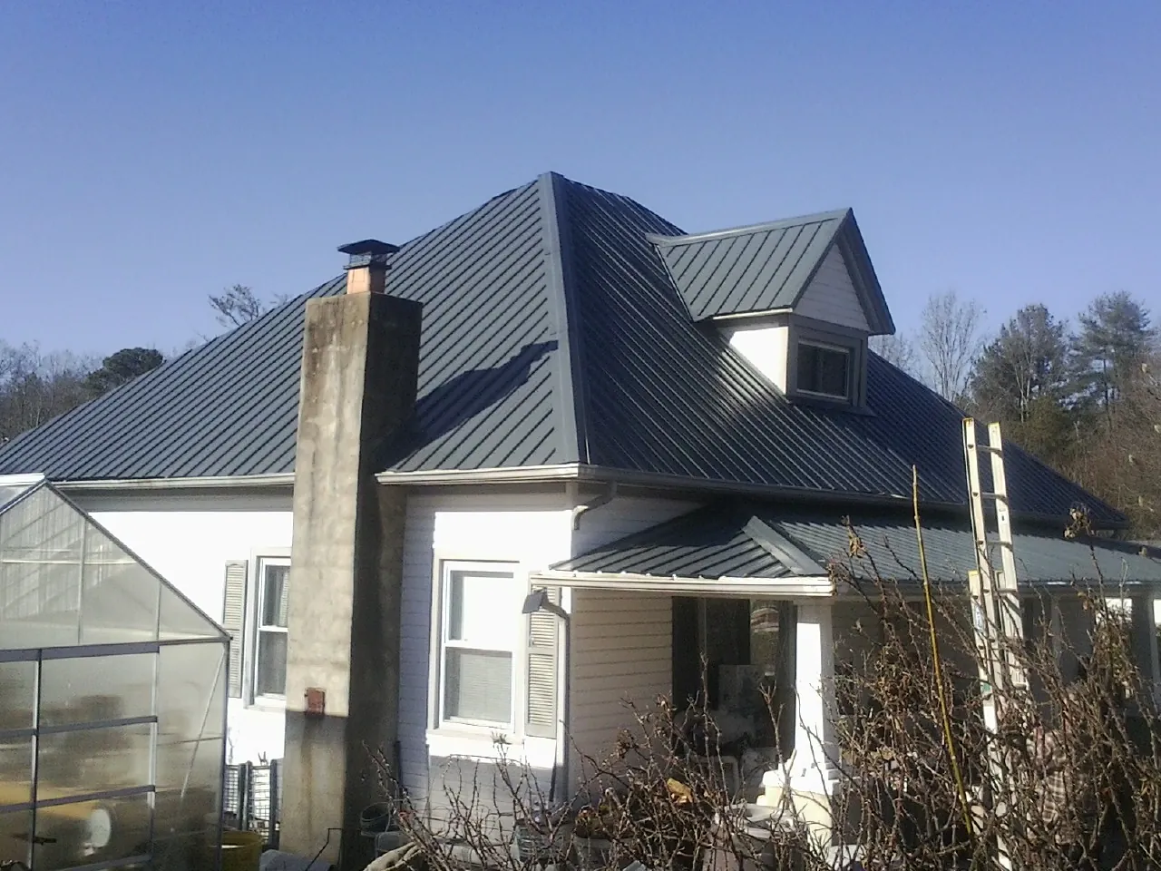 Dark blue standing seam metal roof on a white farmhouse with dormer — Slate & Tile Roof Repair by Roofing Brothers in Derby
