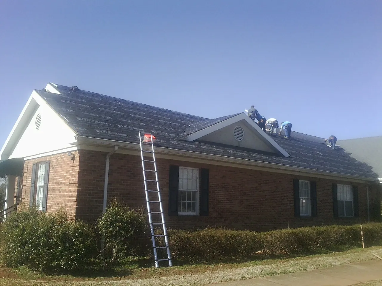Crew tearing shingles off a brick ranch roof with a ladder set — Emergency Roof Repair work by our crew in Derby