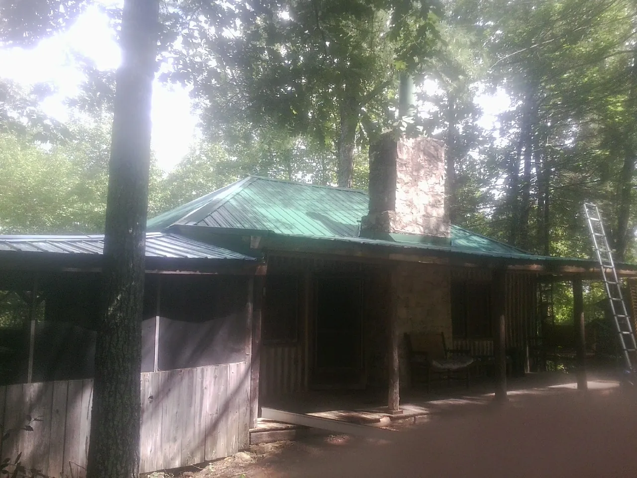 Green metal roof and stone chimney above a log cabin porch in Derby